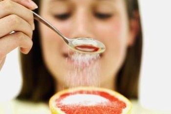 A woman sprinkling sugar on a grapefruit slice — highlighting the hidden sugar we often add to fruits.