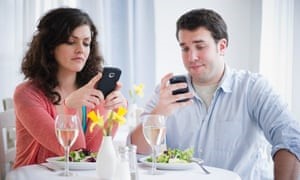 Man and woman distracted by mobile phones while sitting at dining table — highlighting unhealthy eating habits
