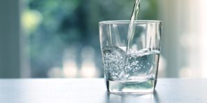 Water being poured into a half-filled glass — symbolizing hydration and healthy weight habits